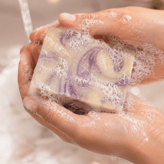 Hand holding a bar of soap with water running over it, surrounded by bubbles.