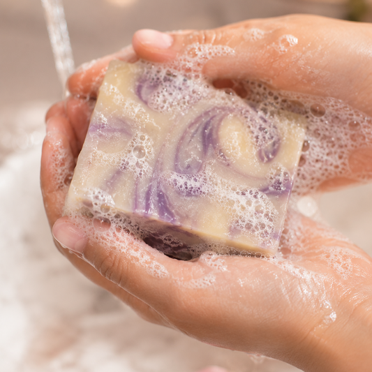 Hand holding a bar of soap with water running over it, surrounded by bubbles.