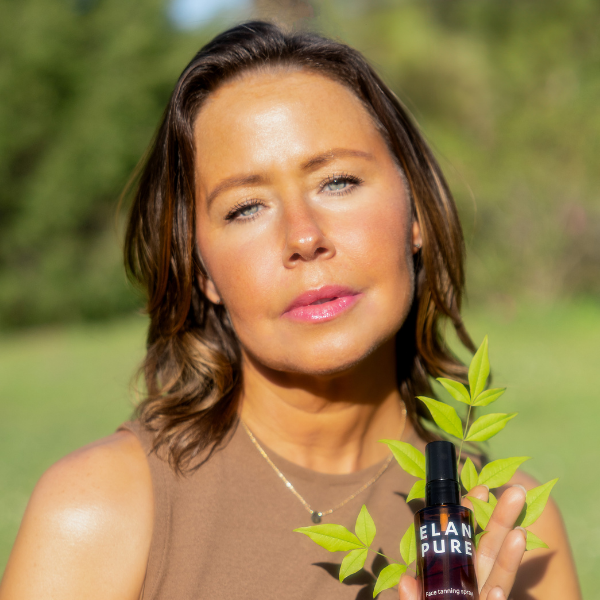 Woman holding a bottle labeled 'ELAN PURE' with greenery in a natural setting